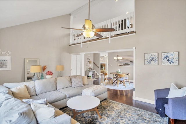 living room featuring high vaulted ceiling, ceiling fan with notable chandelier, wood finished floors, baseboards, and stairway