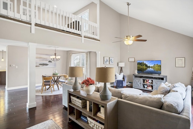 living room with dark wood-type flooring, high vaulted ceiling, ornate columns, and ceiling fan with notable chandelier