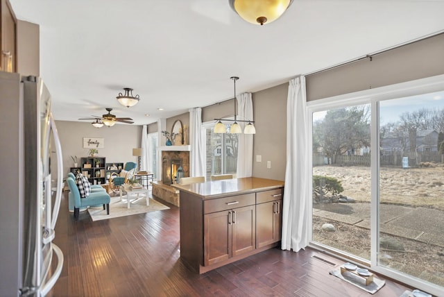 kitchen with a peninsula, dark wood-type flooring, a lit fireplace, hanging light fixtures, and freestanding refrigerator