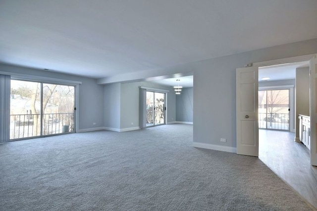 carpeted empty room featuring an inviting chandelier and baseboards