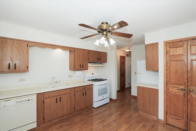 kitchen featuring white appliances, brown cabinetry, wood finished floors, under cabinet range hood, and a sink