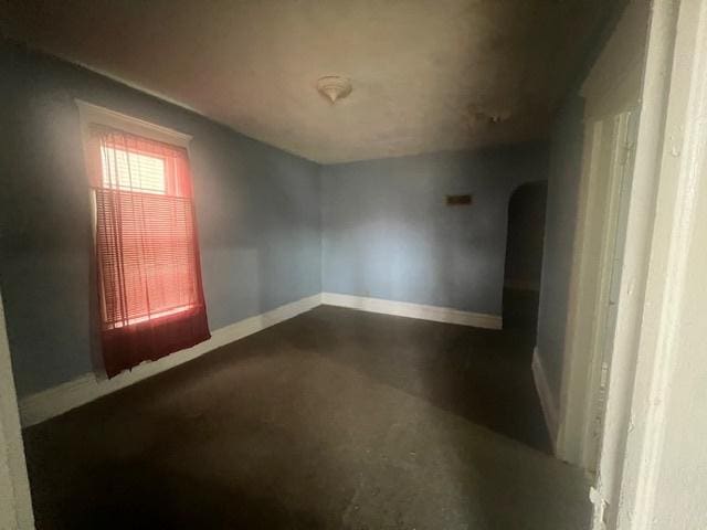 empty room featuring concrete floors, baseboards, and arched walkways