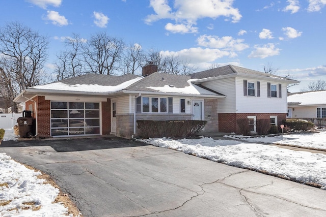 split level home featuring an attached garage, brick siding, a shingled roof, driveway, and a chimney