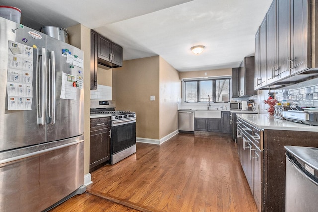 kitchen with wood finished floors, dark brown cabinets, appliances with stainless steel finishes, and a sink