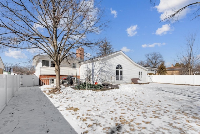 snow covered property featuring a fenced backyard, a chimney, a gate, and brick siding