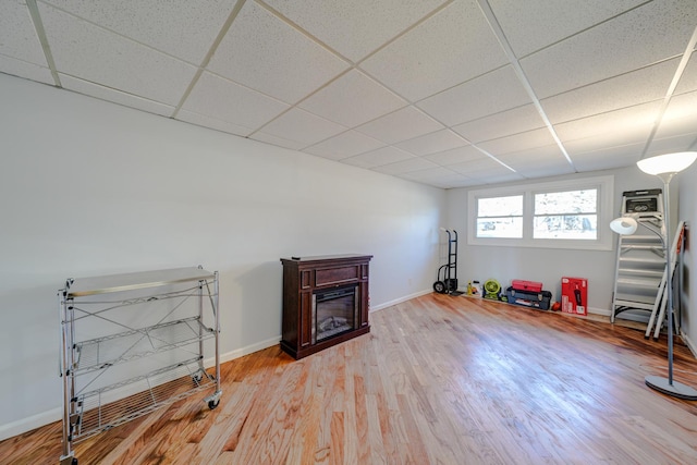 playroom featuring light wood-style floors, baseboards, a drop ceiling, and a glass covered fireplace
