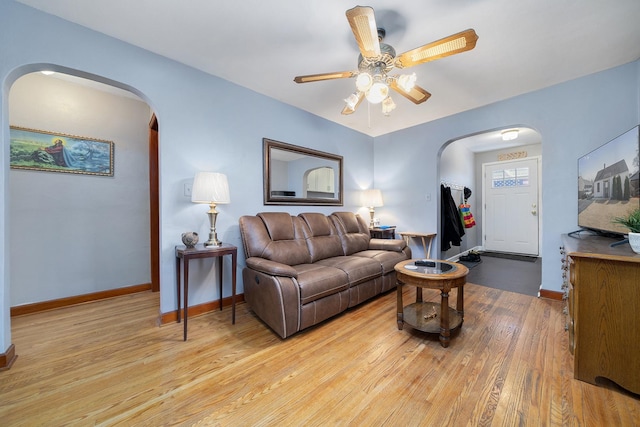 living area featuring arched walkways, ceiling fan, light wood-style flooring, and baseboards