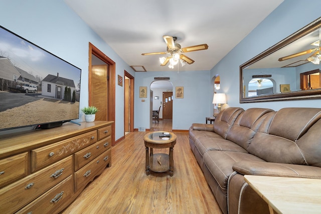 living room featuring arched walkways, ceiling fan, light wood-style flooring, visible vents, and baseboards