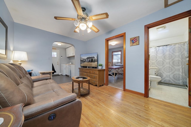 living area featuring visible vents, arched walkways, baseboards, a ceiling fan, and light wood-style floors