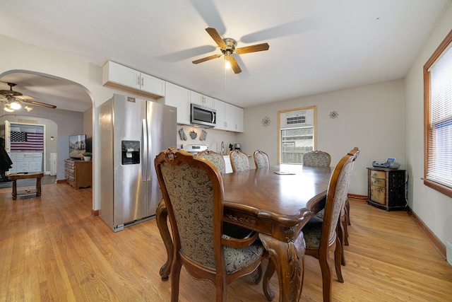 dining area featuring a ceiling fan, arched walkways, light wood-style flooring, and baseboards