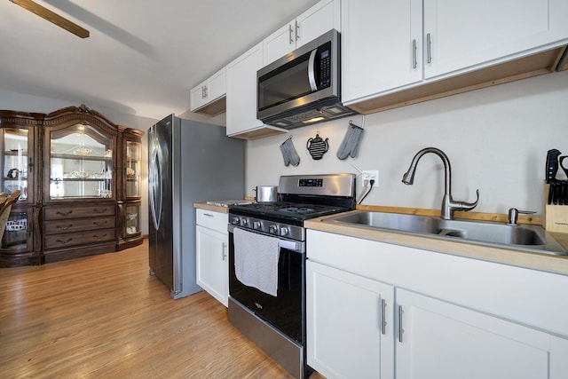 kitchen with white cabinets, appliances with stainless steel finishes, light countertops, light wood-type flooring, and a sink