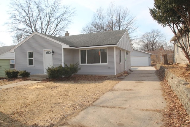 view of front facade with roof with shingles, a chimney, a detached garage, and an outdoor structure