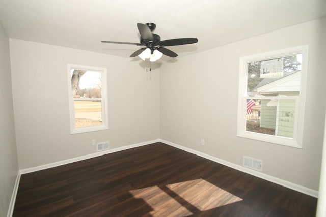 empty room featuring dark wood-type flooring, visible vents, and baseboards