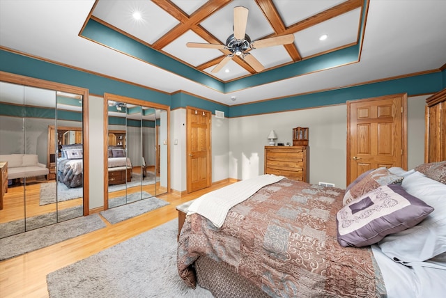 bedroom featuring multiple closets, ornamental molding, wood finished floors, coffered ceiling, and baseboards