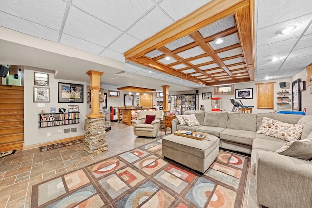 living room with ornate columns, stone tile floors, baseboards, and a drop ceiling