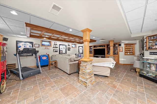 living area with decorative columns, baseboards, visible vents, a drop ceiling, and stone finish floor