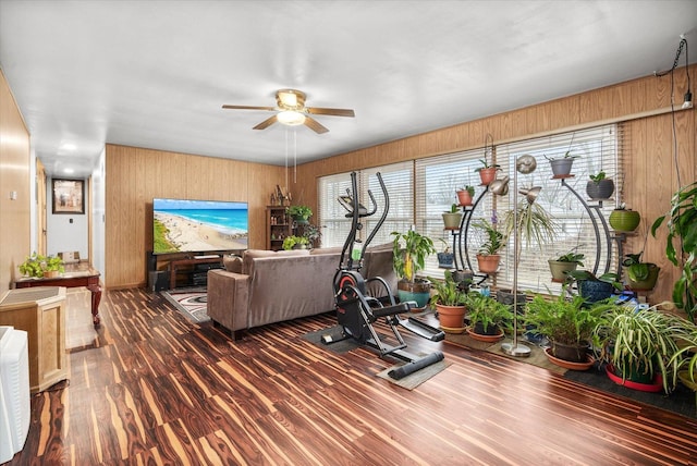 living area with ceiling fan, wood walls, and wood finished floors