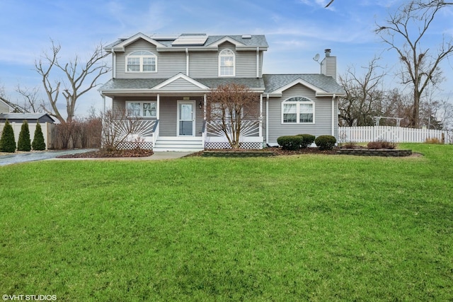 traditional-style house with covered porch, fence, roof mounted solar panels, and a front lawn