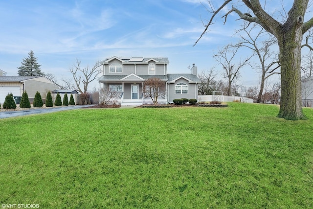 traditional home with driveway, a chimney, covered porch, fence, and a front lawn