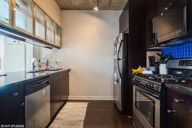 kitchen with a sink, baseboards, appliances with stainless steel finishes, tasteful backsplash, and dark wood finished floors