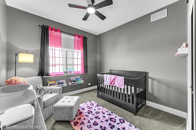 carpeted bedroom featuring a ceiling fan, visible vents, a crib, and baseboards