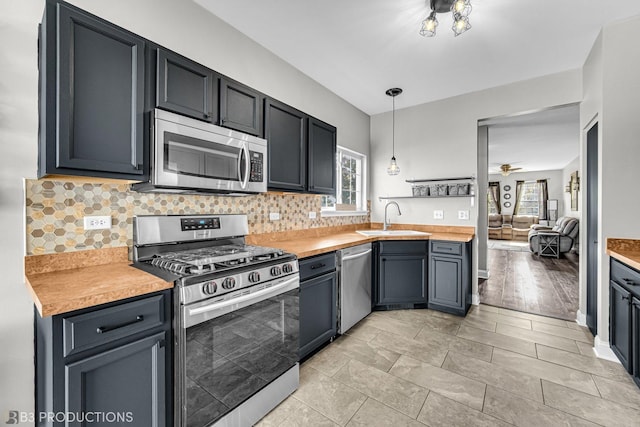 kitchen with light countertops, hanging light fixtures, backsplash, appliances with stainless steel finishes, and a sink