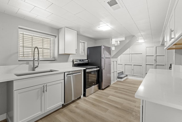 kitchen with light wood finished floors, light countertops, appliances with stainless steel finishes, white cabinets, and a sink