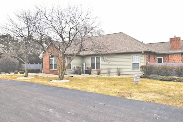 ranch-style home featuring a shingled roof, fence, and a front lawn