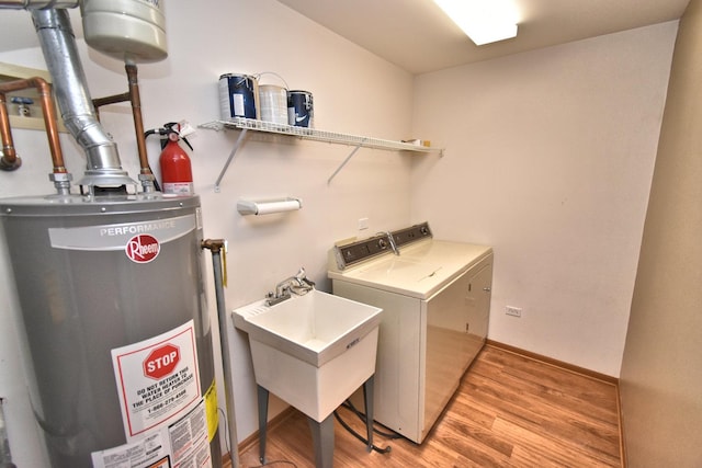 laundry area with laundry area, light wood finished floors, gas water heater, washer and clothes dryer, and a sink