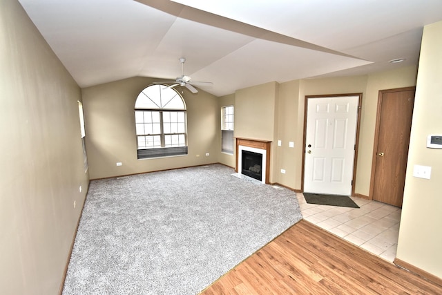 unfurnished living room with a fireplace with flush hearth, a ceiling fan, baseboards, vaulted ceiling, and light wood-style floors