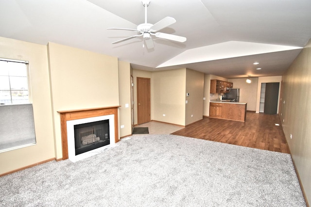 unfurnished living room featuring ceiling fan, a fireplace, wood finished floors, baseboards, and vaulted ceiling