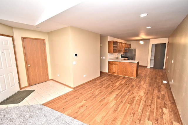 kitchen featuring brown cabinets, open shelves, freestanding refrigerator, a sink, and a peninsula