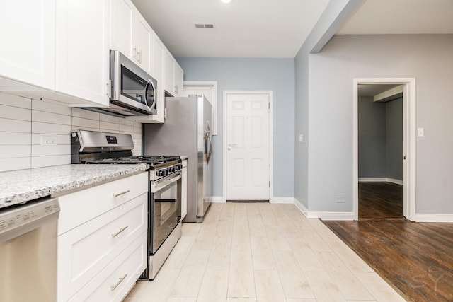 kitchen with stainless steel appliances, visible vents, backsplash, white cabinets, and light stone countertops