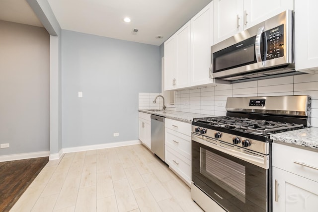 kitchen with baseboards, decorative backsplash, light stone counters, appliances with stainless steel finishes, and a sink