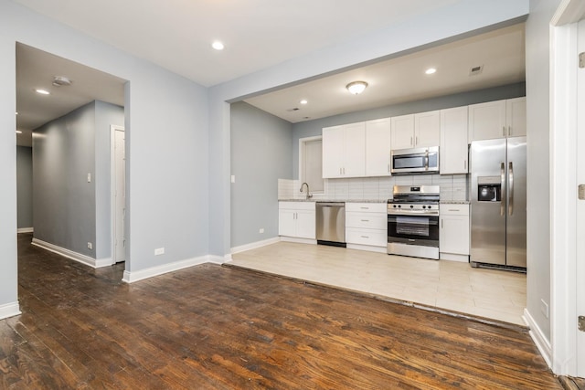 kitchen featuring tasteful backsplash, appliances with stainless steel finishes, white cabinets, a sink, and wood finished floors