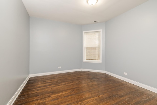 unfurnished room with dark wood-style flooring, visible vents, and baseboards