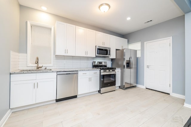 kitchen featuring tasteful backsplash, visible vents, white cabinets, stainless steel appliances, and a sink