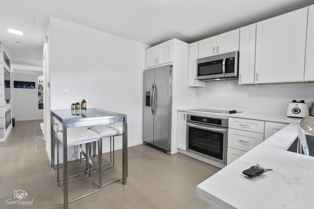 kitchen featuring baseboards, appliances with stainless steel finishes, light stone counters, light wood-type flooring, and white cabinetry