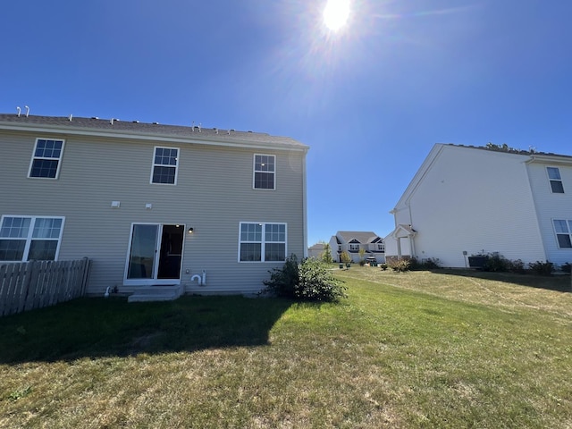 rear view of property with entry steps, a yard, and fence