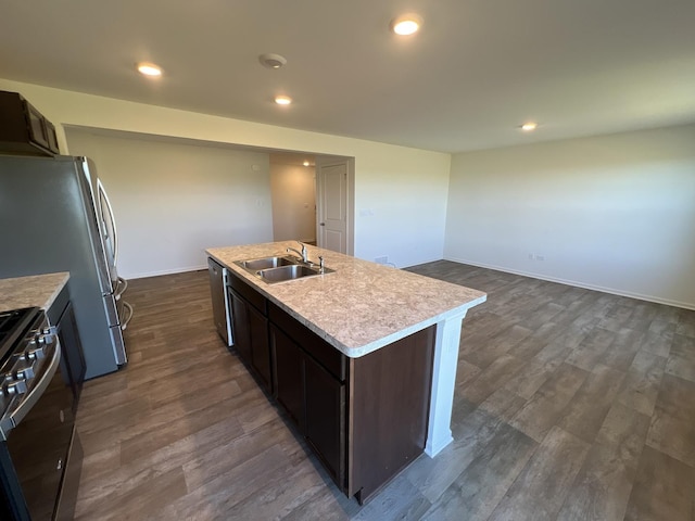 kitchen with a sink, light countertops, appliances with stainless steel finishes, dark wood-style floors, and a kitchen island with sink