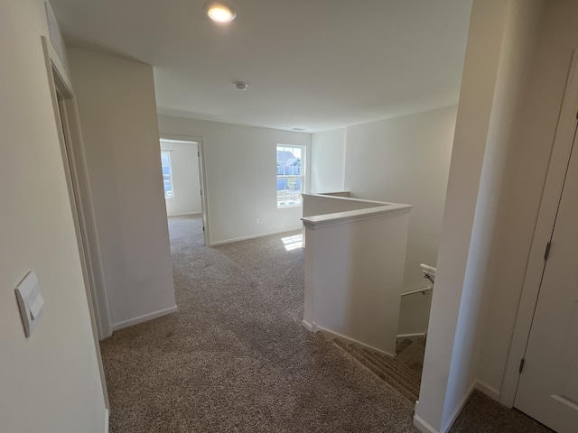 hallway featuring an upstairs landing, baseboards, and carpet