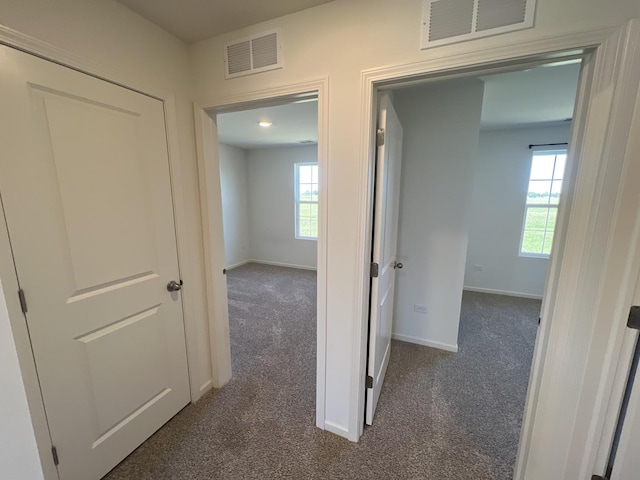 hall with baseboards, visible vents, and dark colored carpet