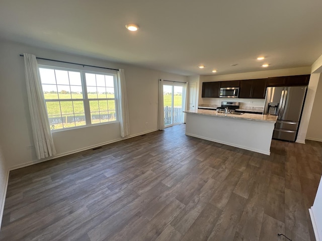 kitchen featuring dark wood-type flooring, a center island with sink, recessed lighting, appliances with stainless steel finishes, and baseboards