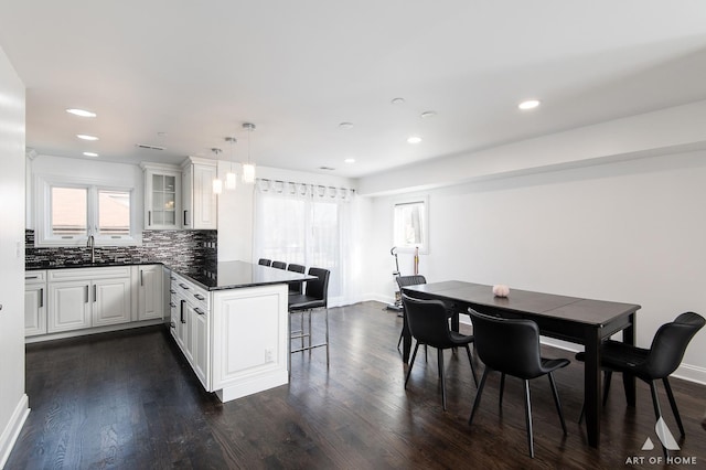 kitchen with a peninsula, dark wood-type flooring, decorative backsplash, dark countertops, and glass insert cabinets