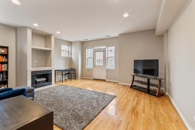 living area with light wood finished floors, recessed lighting, a fireplace with flush hearth, and baseboards