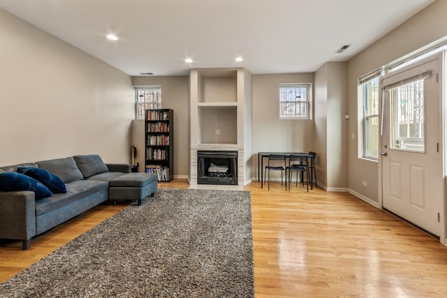 living room with recessed lighting, a fireplace with flush hearth, visible vents, baseboards, and light wood-type flooring