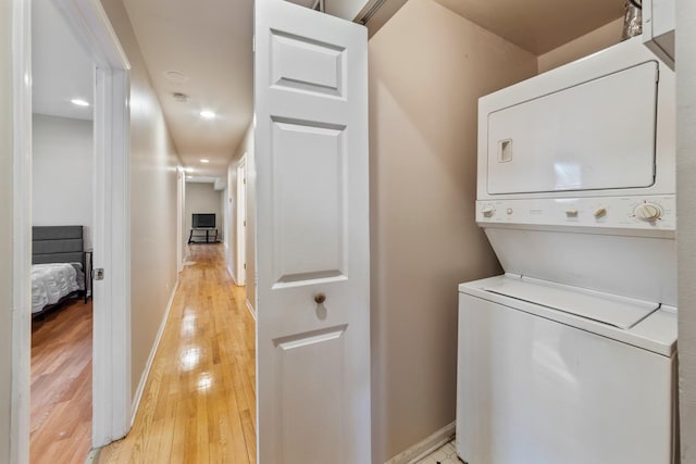 laundry area featuring laundry area, light wood finished floors, stacked washer and clothes dryer, and baseboards