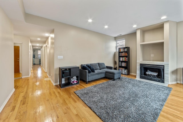 living area with baseboards, built in features, light wood-style flooring, a fireplace with flush hearth, and recessed lighting