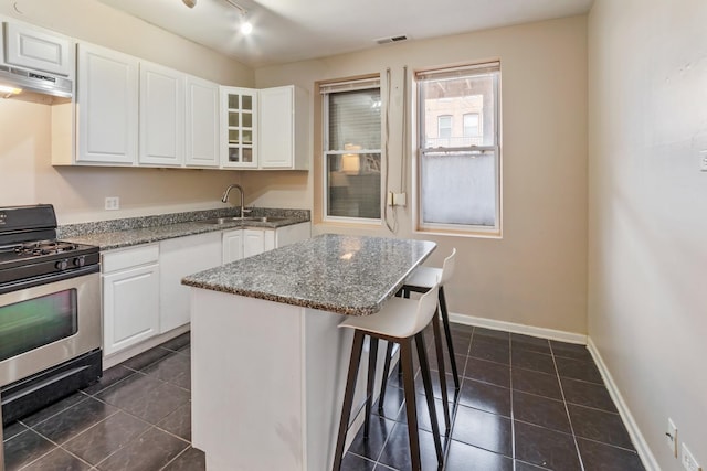 kitchen featuring under cabinet range hood, a sink, white cabinets, a kitchen breakfast bar, and gas stove