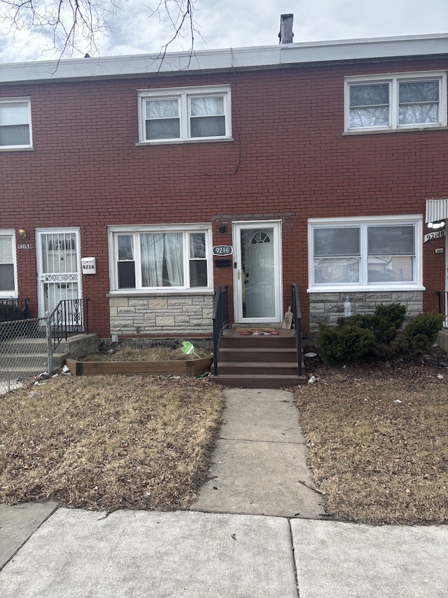 townhome / multi-family property with stone siding, fence, and brick siding